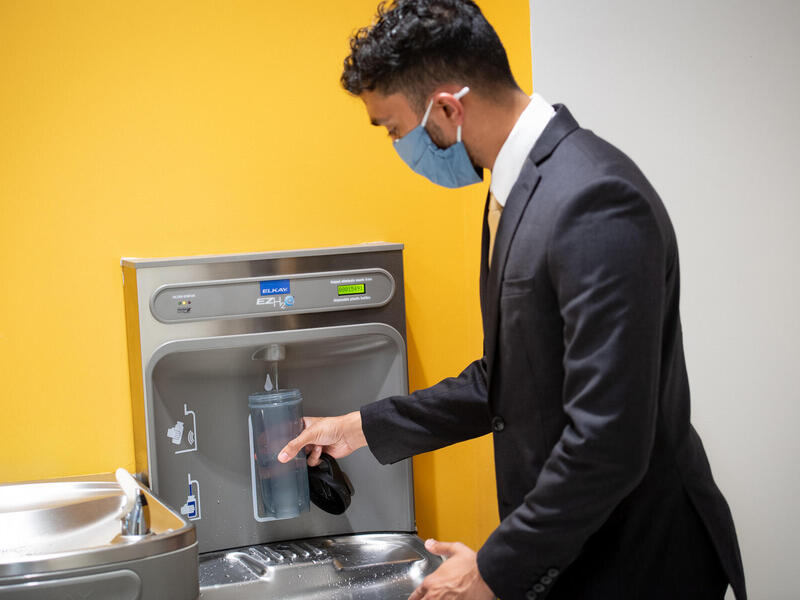 a man in a suit fills a water bottle at a bottle filling station inside a VCU building