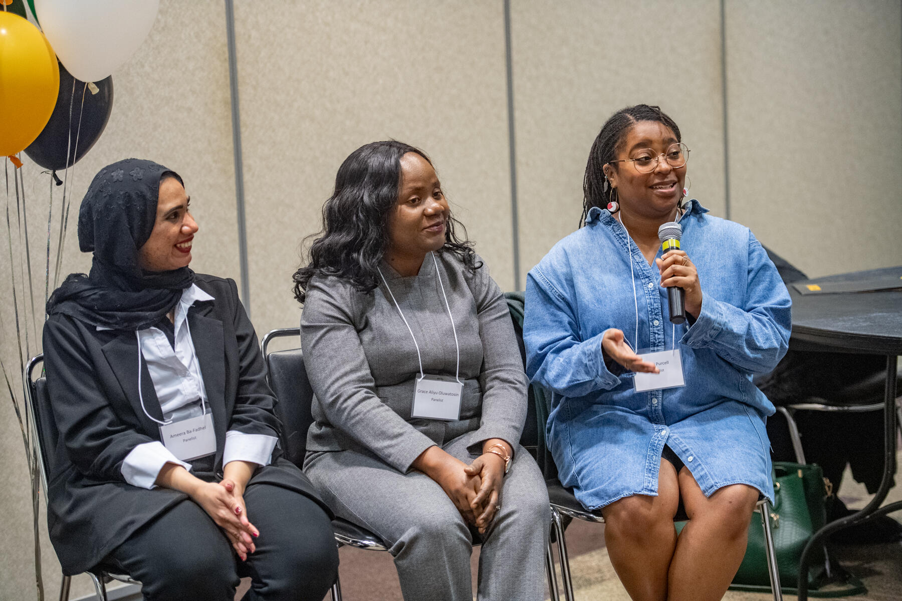 Three women sit side by side. The one on the far right speaks into a microphone.