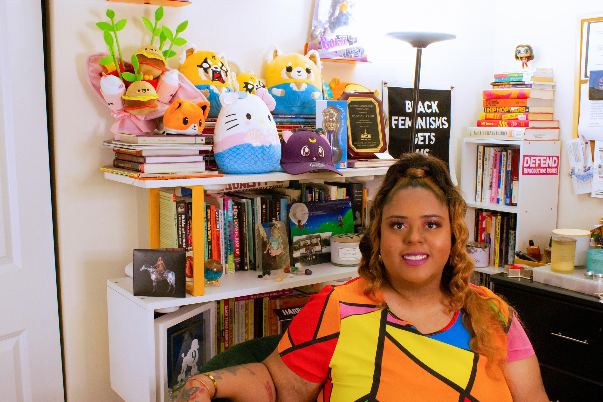 A woman siting in an office filled with books and stuffed toys. 