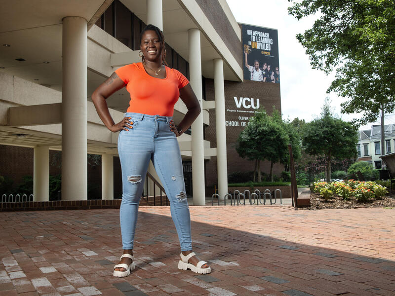 A photo of a woman with her hands on her hips standing in front of the VCU School of Education building and smiling. 