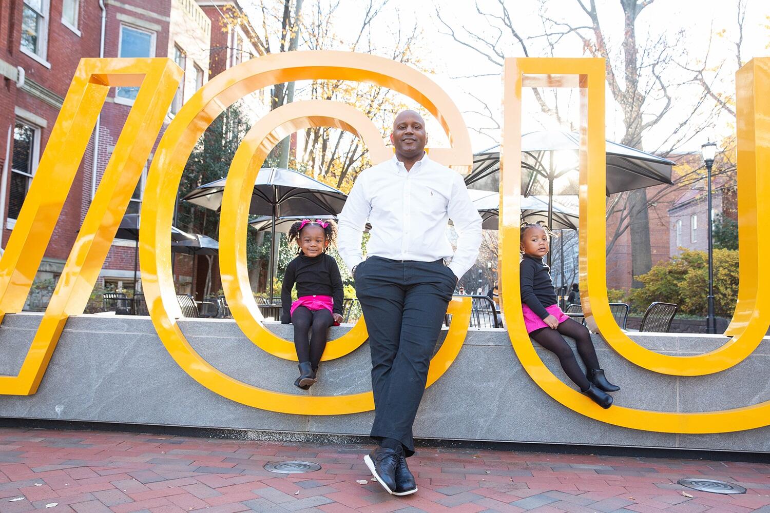 LeQuan Hylton sitting in the middle with daughters Carter (left) and Emory (right) on a VCU sign