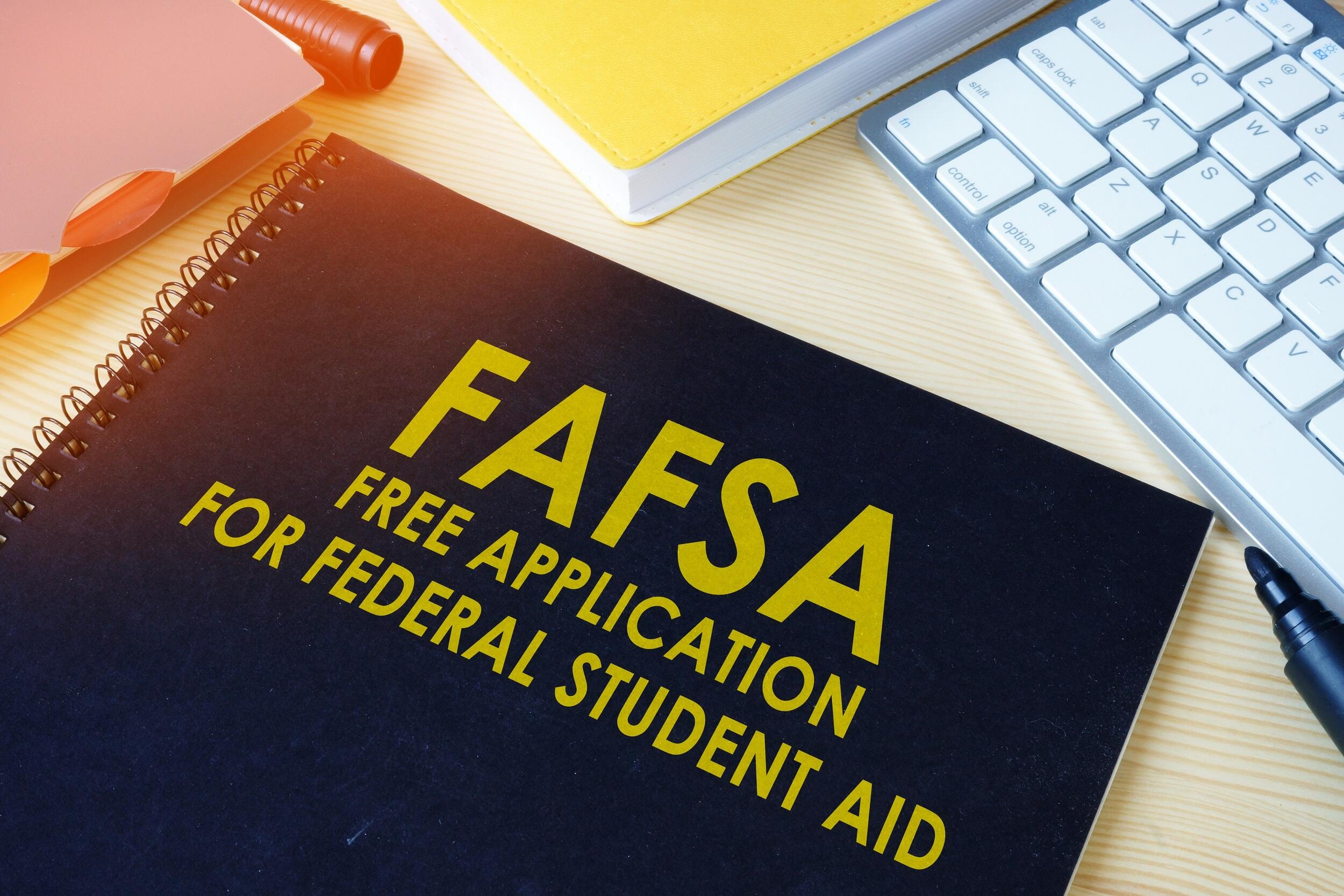 A photo of a black notebook sitting on a table. The front of the notebooks says \"FAFSA FREE APPLICATION FOR FEDERAL STUDENT AID\" in yellow letters