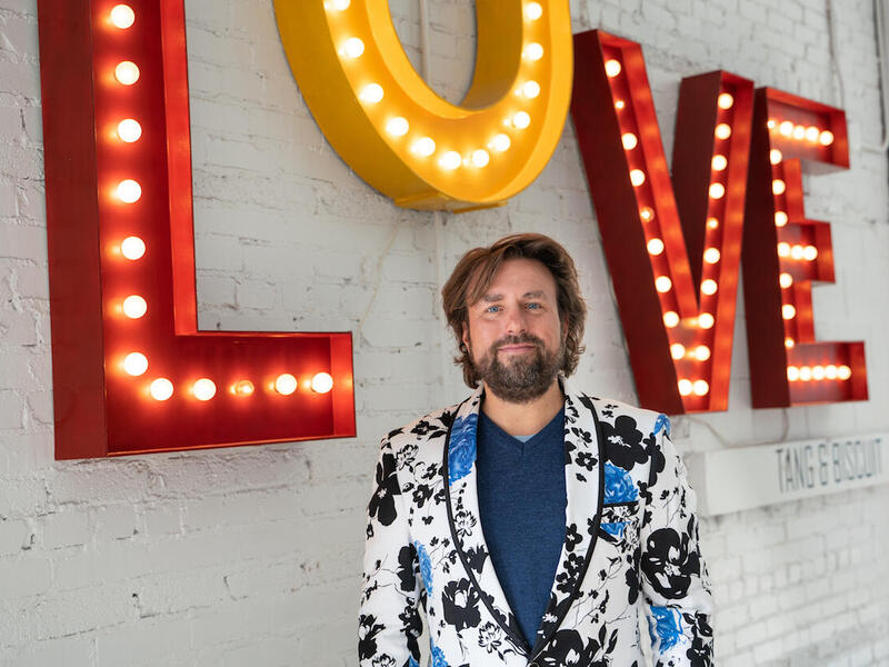 David Gallagher standing in front of wall and lighted sign spelling \"love.\"