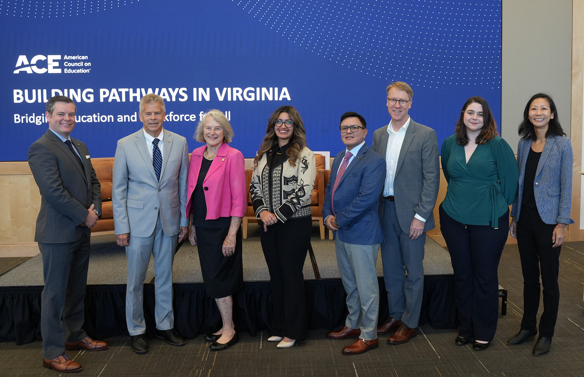 A row of eight people stand in front of a blue sign.