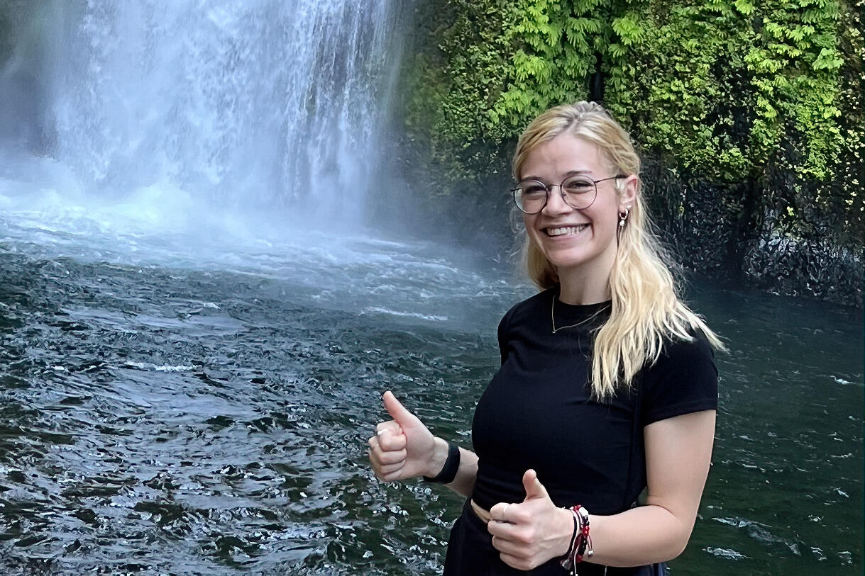 A woman standing in front of a waterfall giving two thumbs up. 