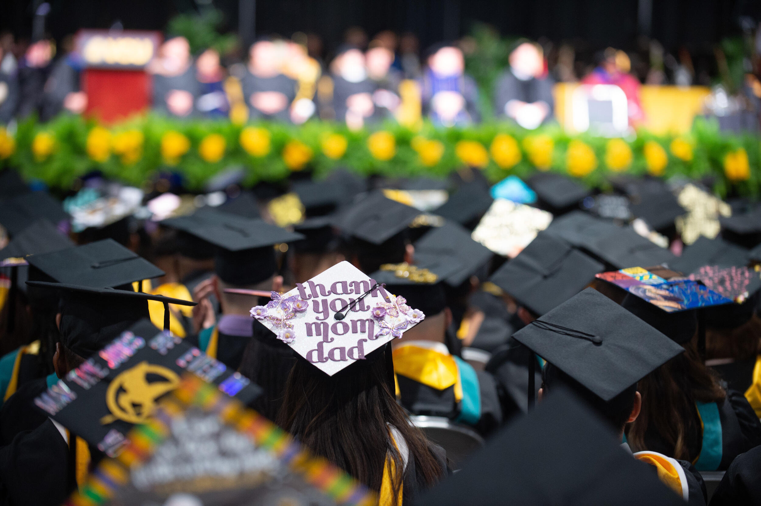 Students wearing graduation caps attend a graduation ceremony. A cap in the foreground says \"thank you mom dad.\"