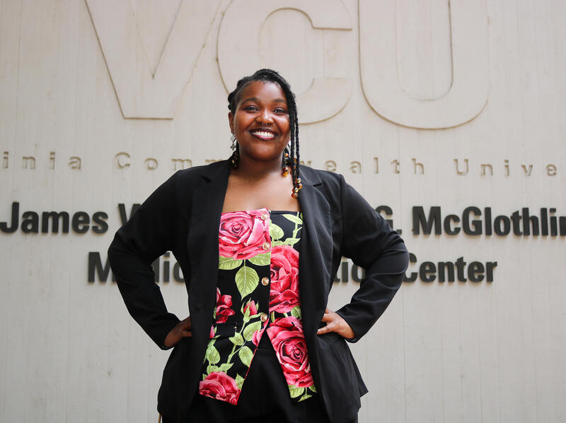 A photo of a woman from the waist up. She's standing with her hands on her hips. 