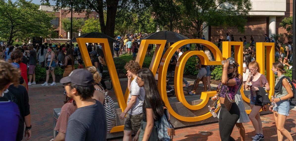People walking past a sculpture of the letters \"VCU.\" 