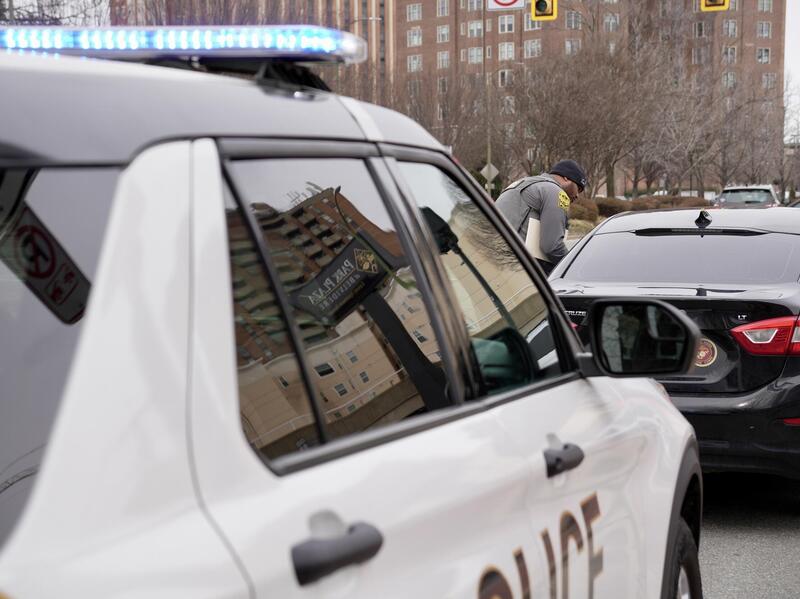 A photo of a police car parked behind a black sedan. A police officer is standing on the driver side of the black car. 