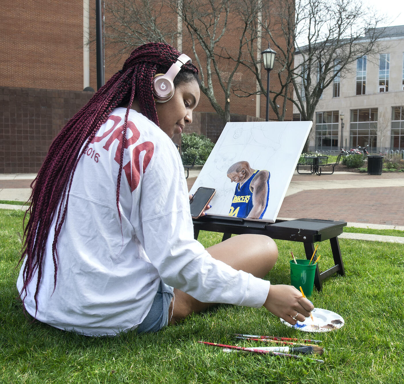 A student sitting in the grass on a warm day while painting outside in Park Plaza.