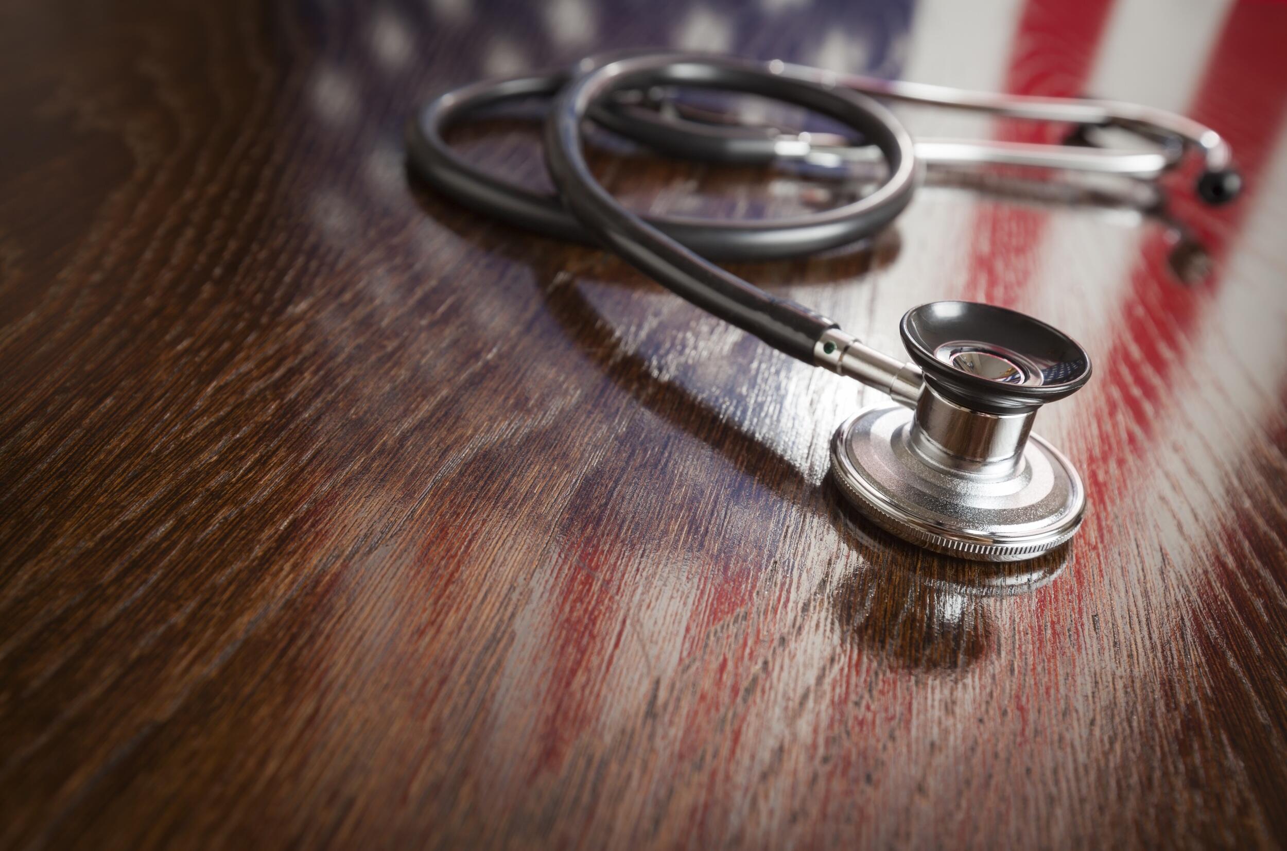 A stethoscope sitting on a wood table with an American Flag