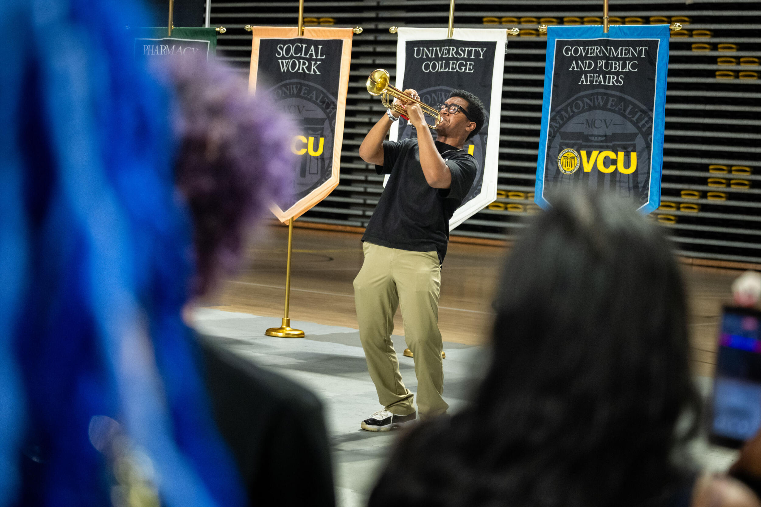 A man in a dark shirt and khakis plays a brass instrument.