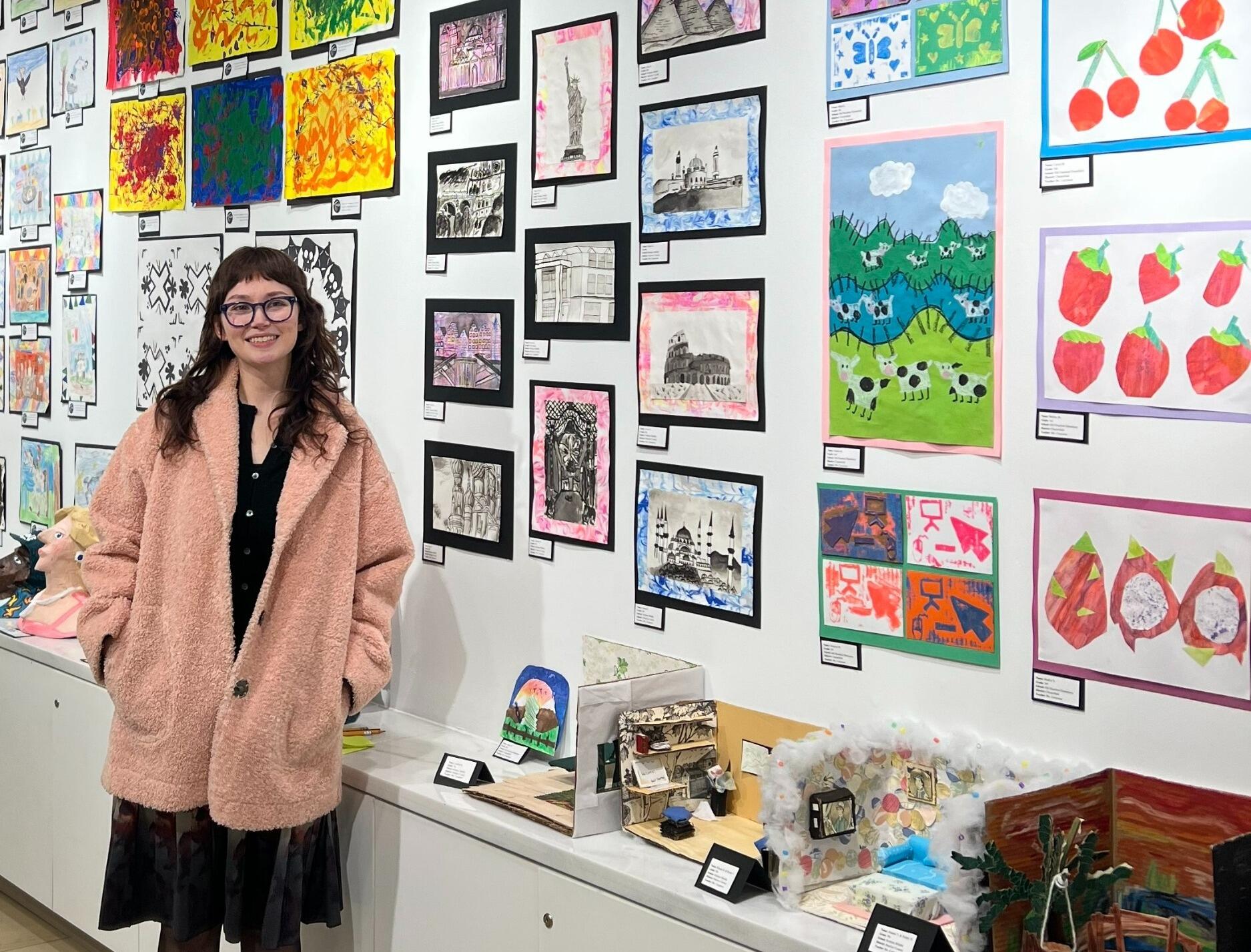 A photo of a woman standing next to a wall covered in several pieces of art. 