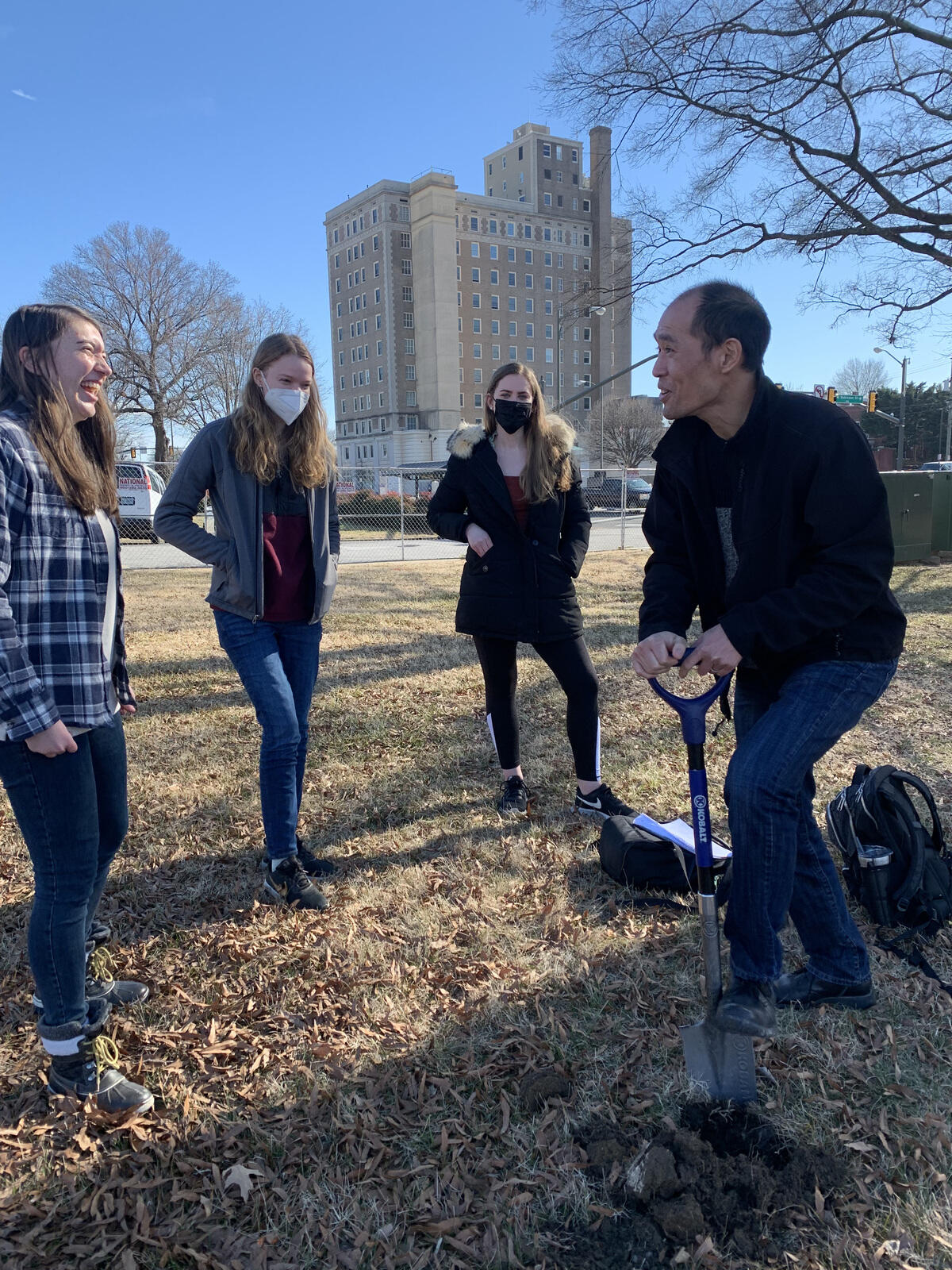 From left, students Emma Gregory, Alexandra Almasy, and Tara Macintosh share a laugh with their professor Stephen Fong, Ph.D., as Fong digs into the ground in front of the Science Museum of Virginia.