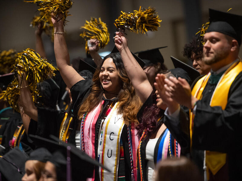 Students in caps and gowns wave pompoms during graduation.