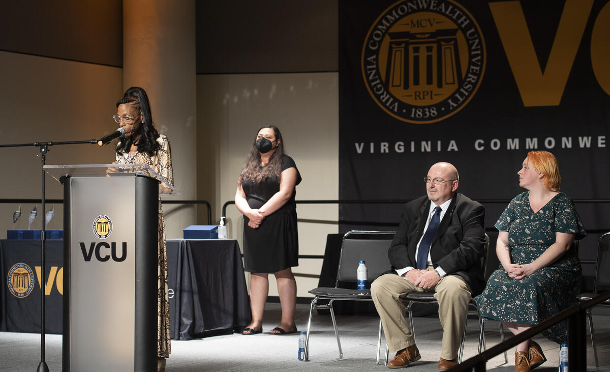 Michele Armstrong, a member of the VCU Staff Senate, speaks at last week's awards. Standing behind her is Saher Randhawa, president of the Staff Senate, and seated are Ken Hudgins, co-chair of the Awards & Recognition Committee, and Brogan King, co-chair of the Awards & Recognition Committee and president-elect for Staff Senate.