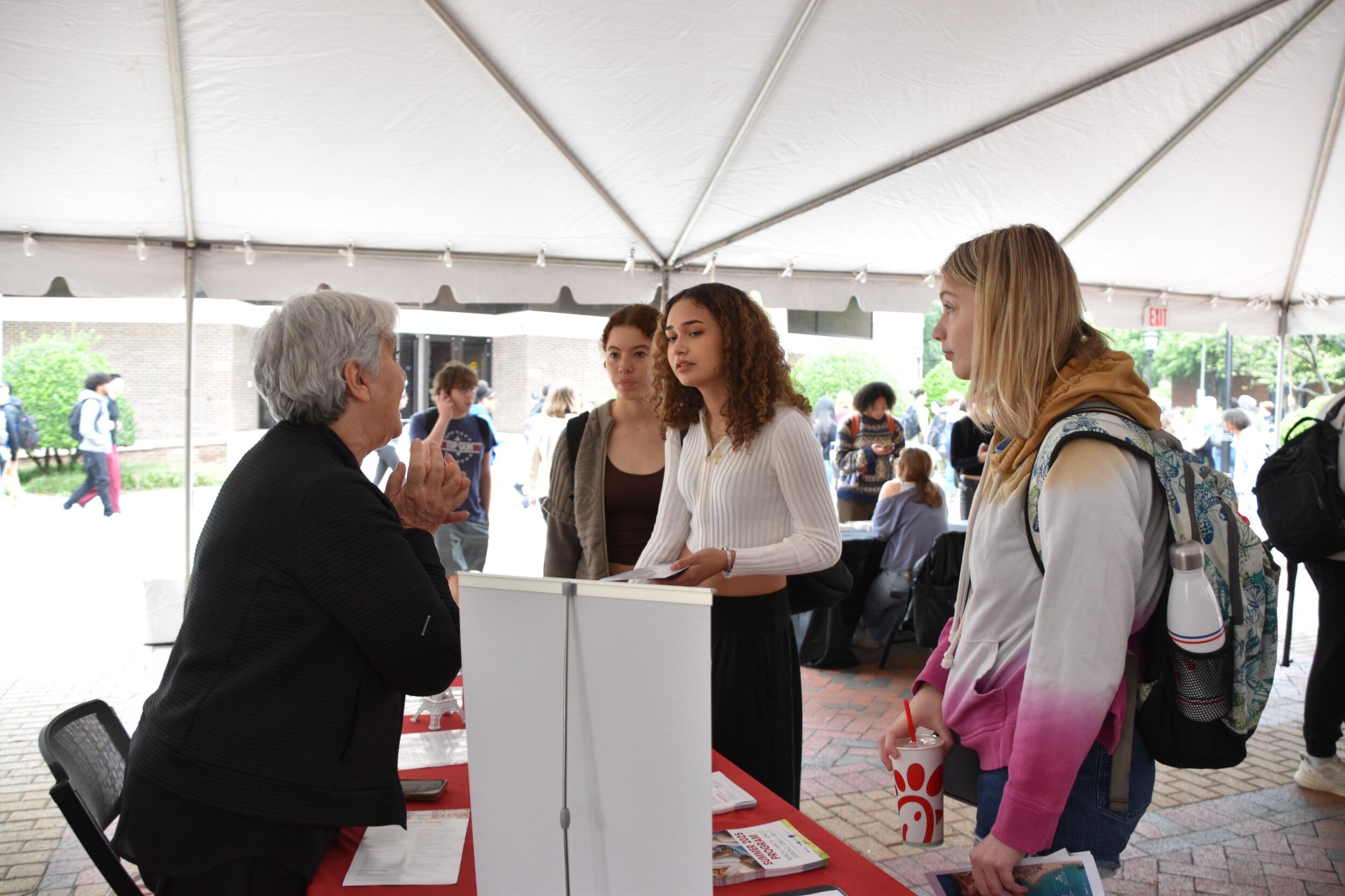 A photo of three students listening to a woman talkin on the other side of a table. 