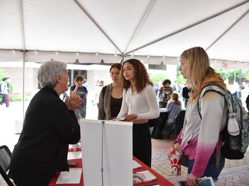 A photo of three students listening to a woman talkin on the other side of a table. 