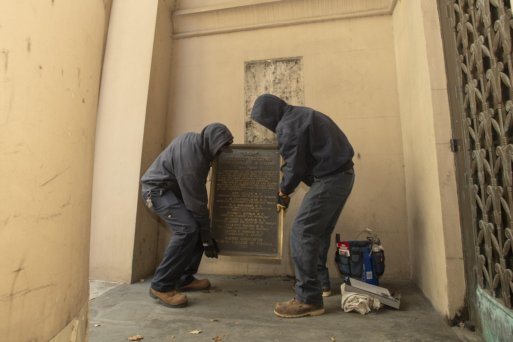 Workers remove a plaque on the Egyptian Building on the MCV Campus commemorating MCV's role in the Civil War. (Tom Kojcsich, University Marketing)