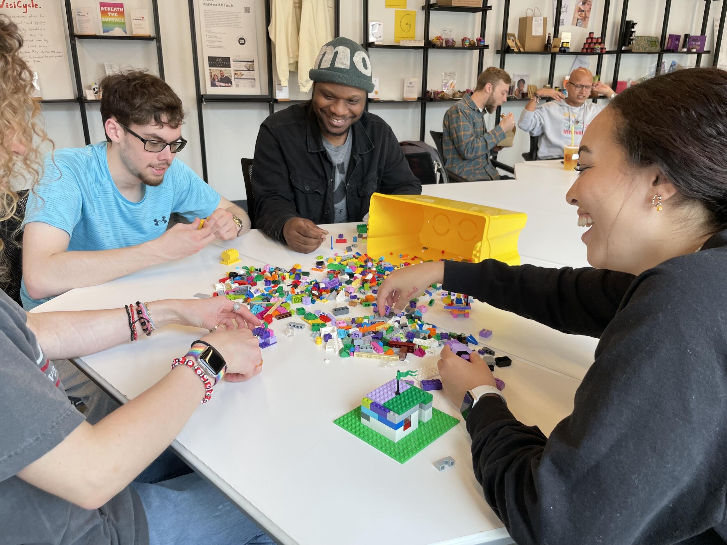 Four people sitting at a white table using LEGO bricks to construct an object. 