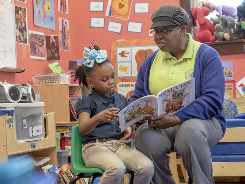 A woman and her daughter are seated in a classroom reading a book.
