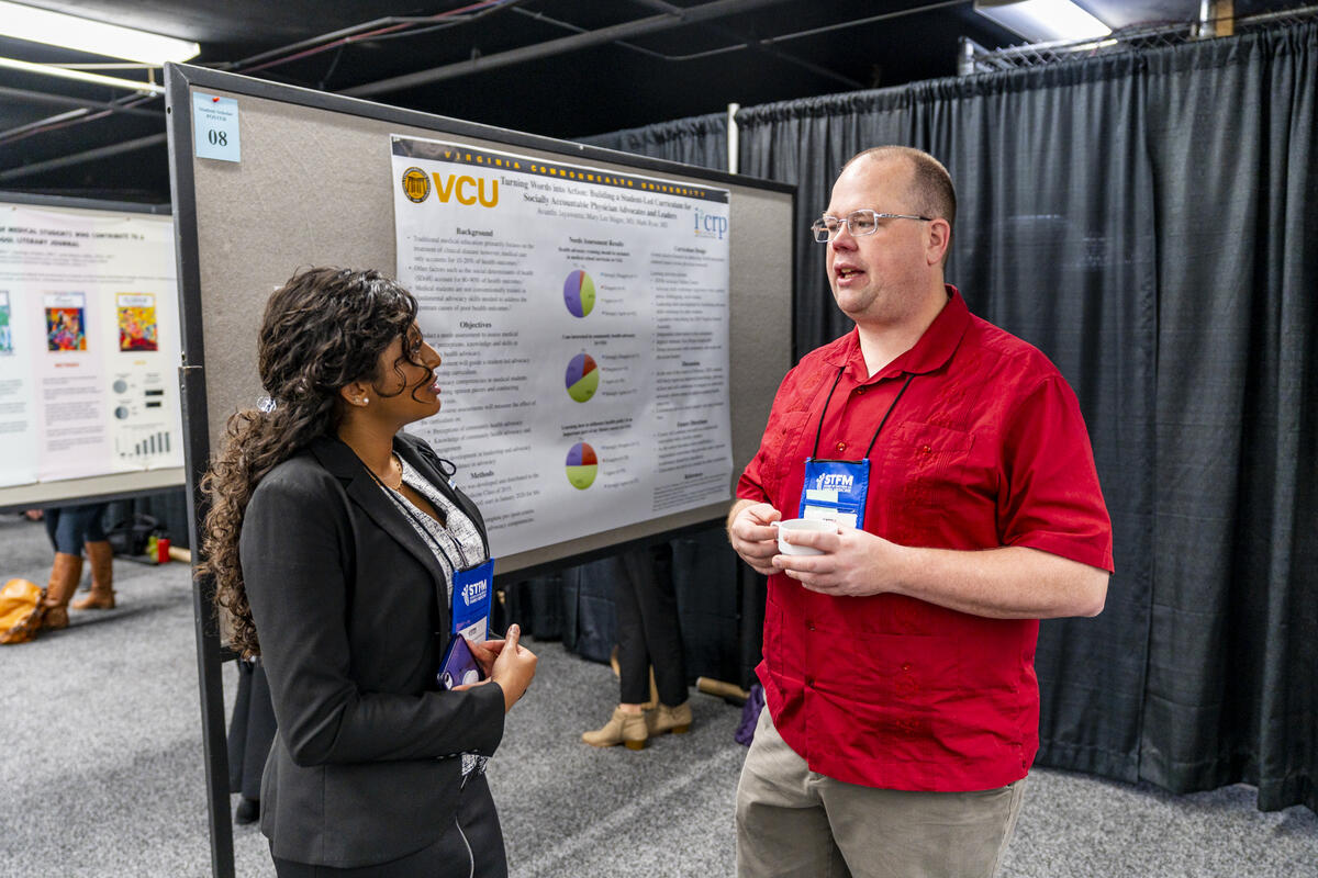 Two people talking to each other in front of a research poster.