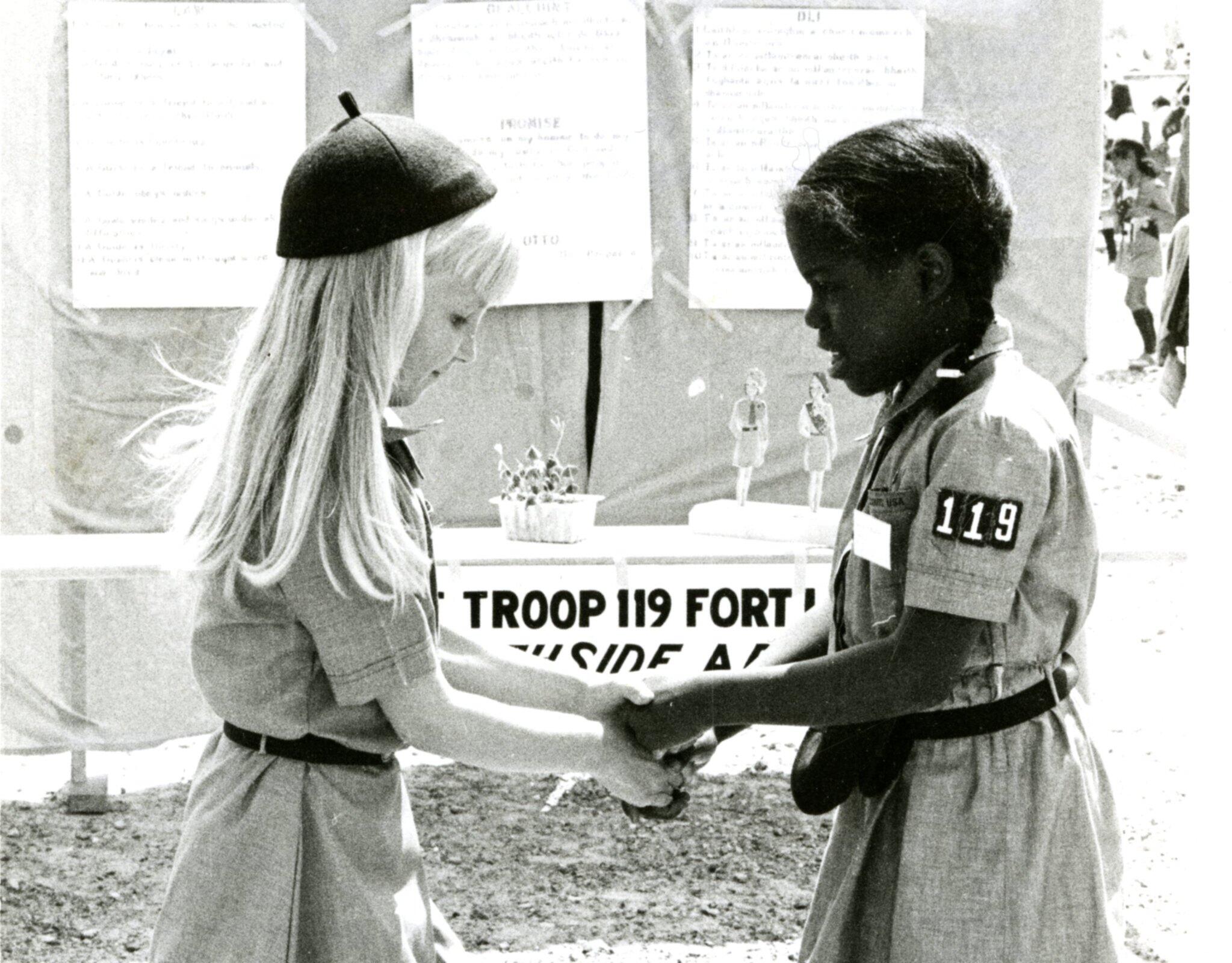 Two little girls wearing girl scout uniforms facing each other and holding hands. 