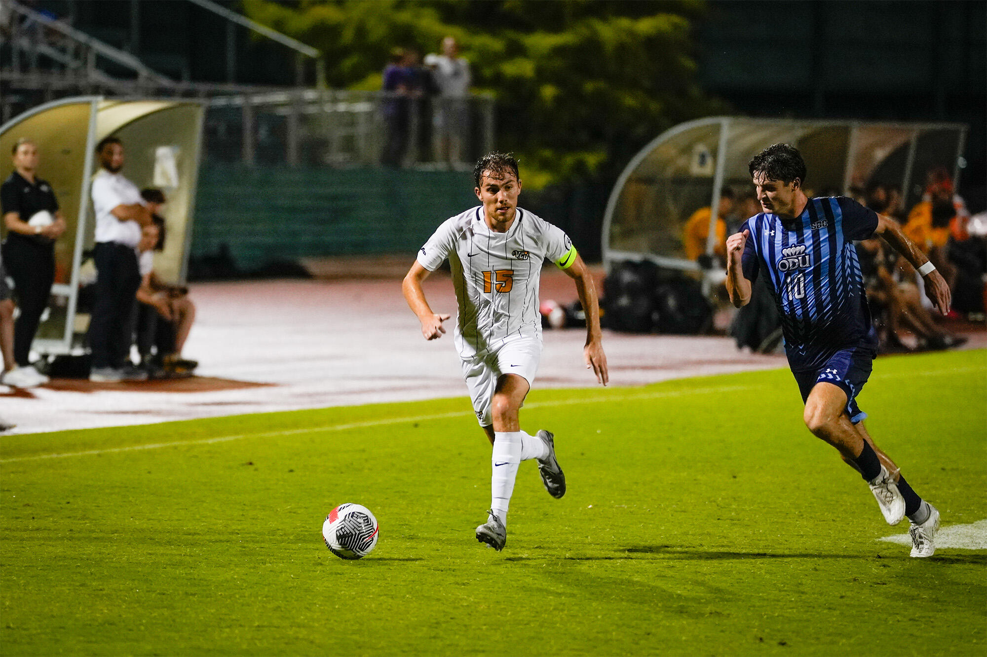 A photo of two men running on a soccer field towards a soccer ball. 