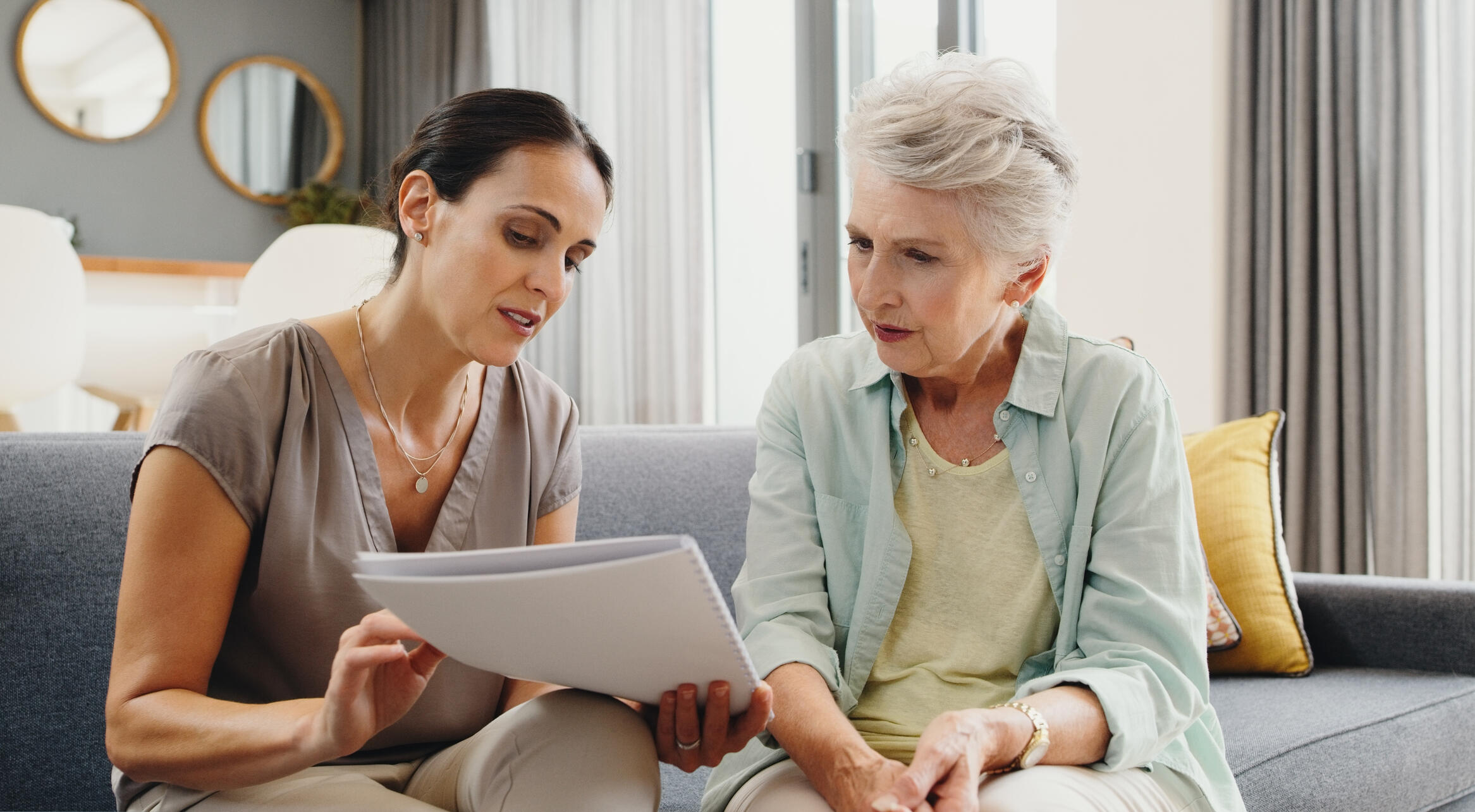 A woman holds a paper out to look at with an older woman.