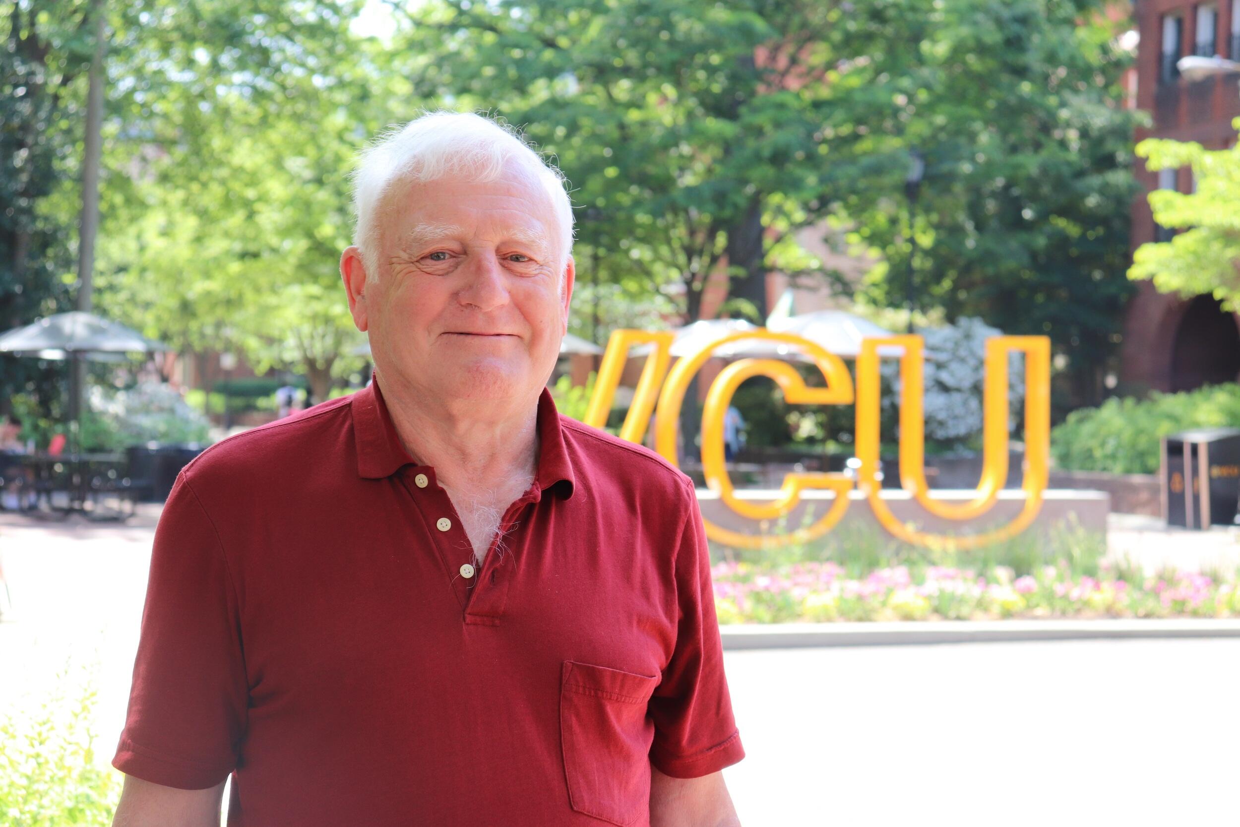 A portrait of a man from the chest up standing outside in front of a sign that says \"VCU\"