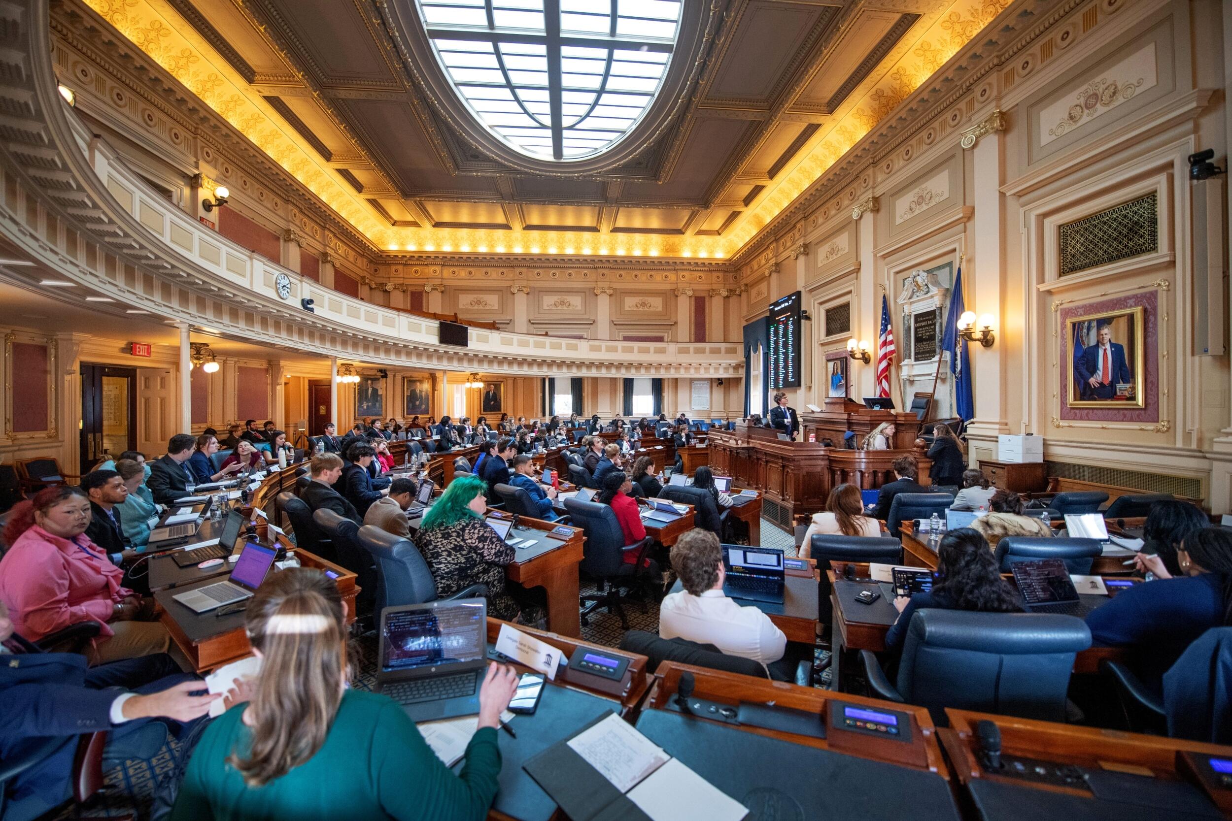 A photo of students sitting in delegates' seats at the Virginia state Capitol’s House of Delegates chamber, 