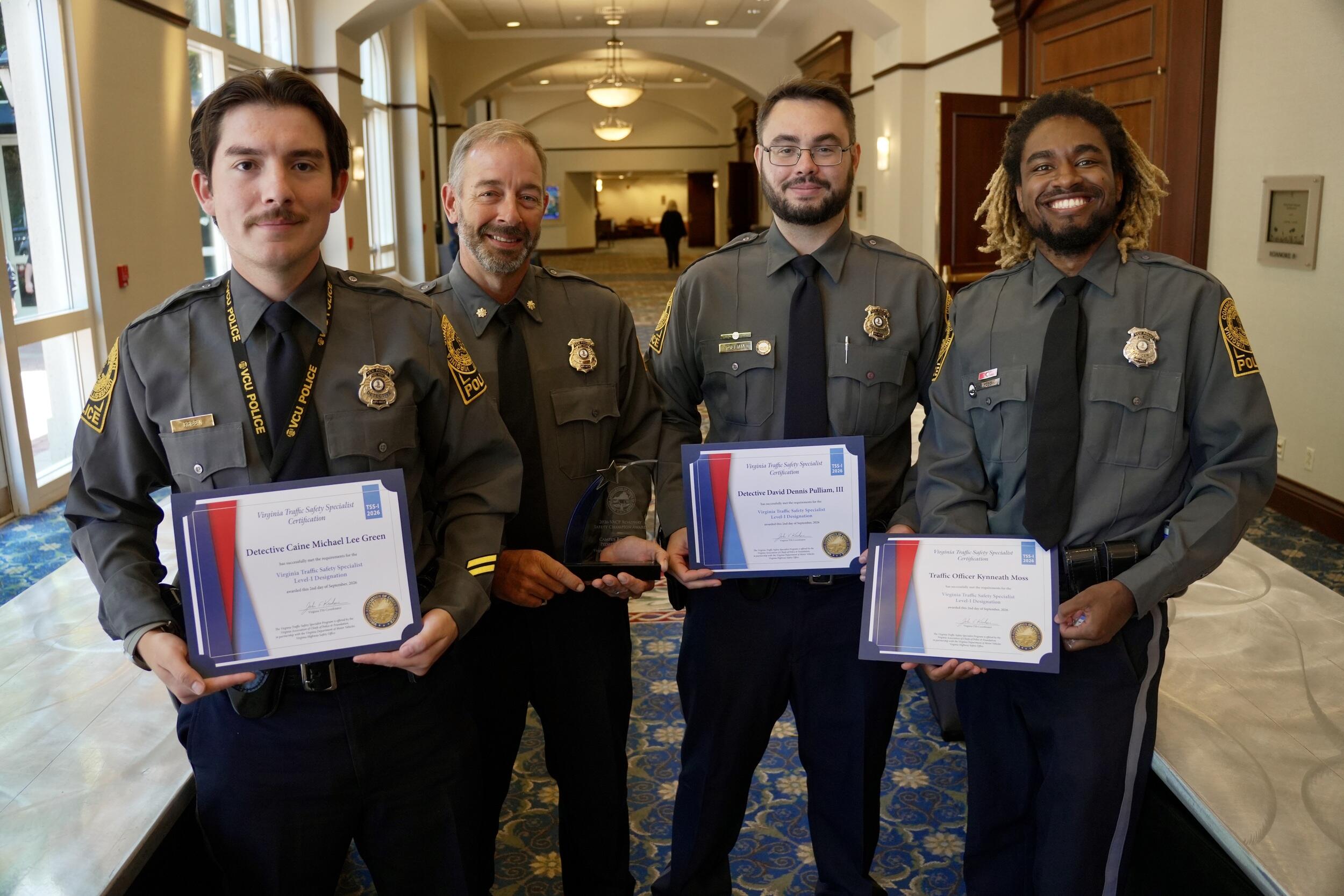 A group photo of four police officers, three are holding certificates.