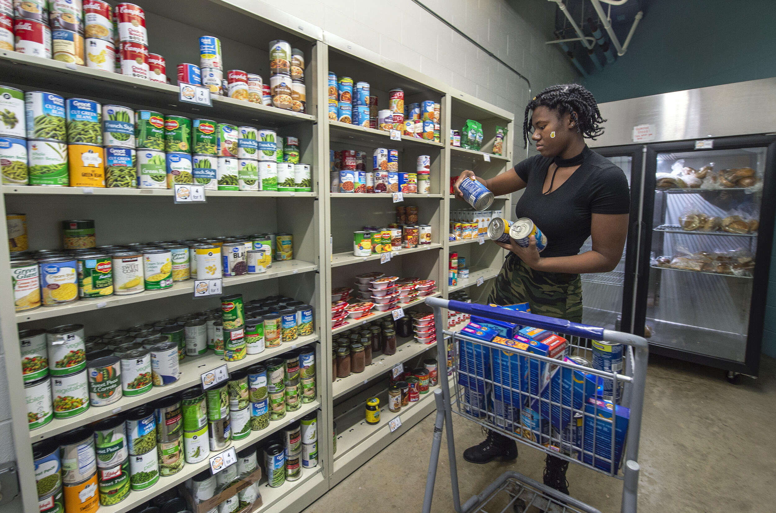 A person reads a can of soup. Donated food items sit on shelves in the background.
