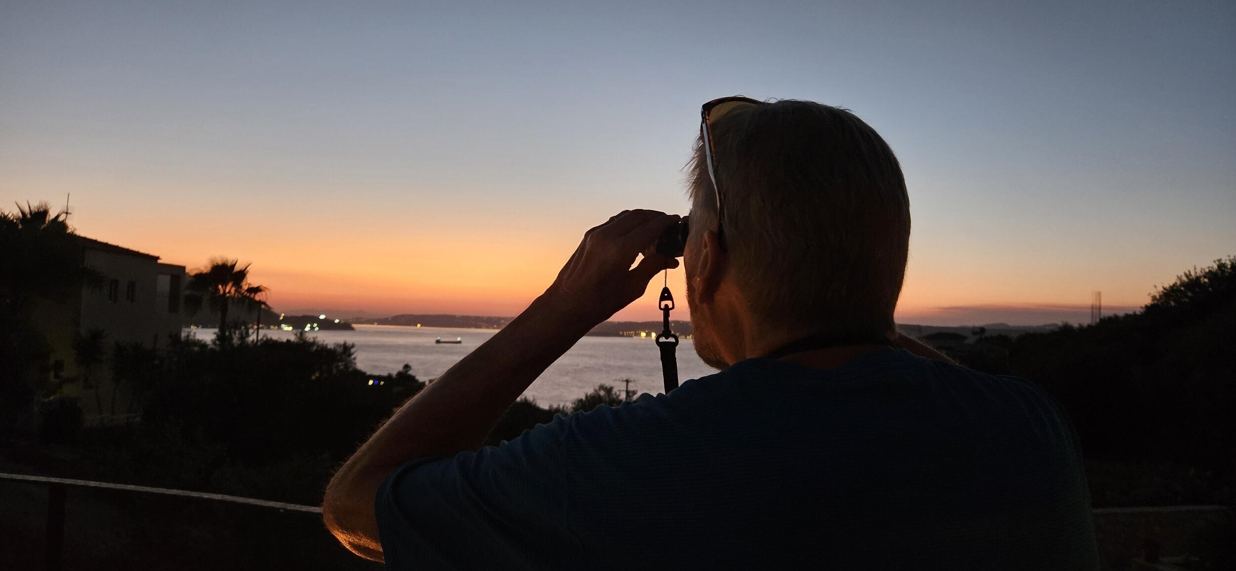 A photo of a man looking out the horizon with binoculars. 