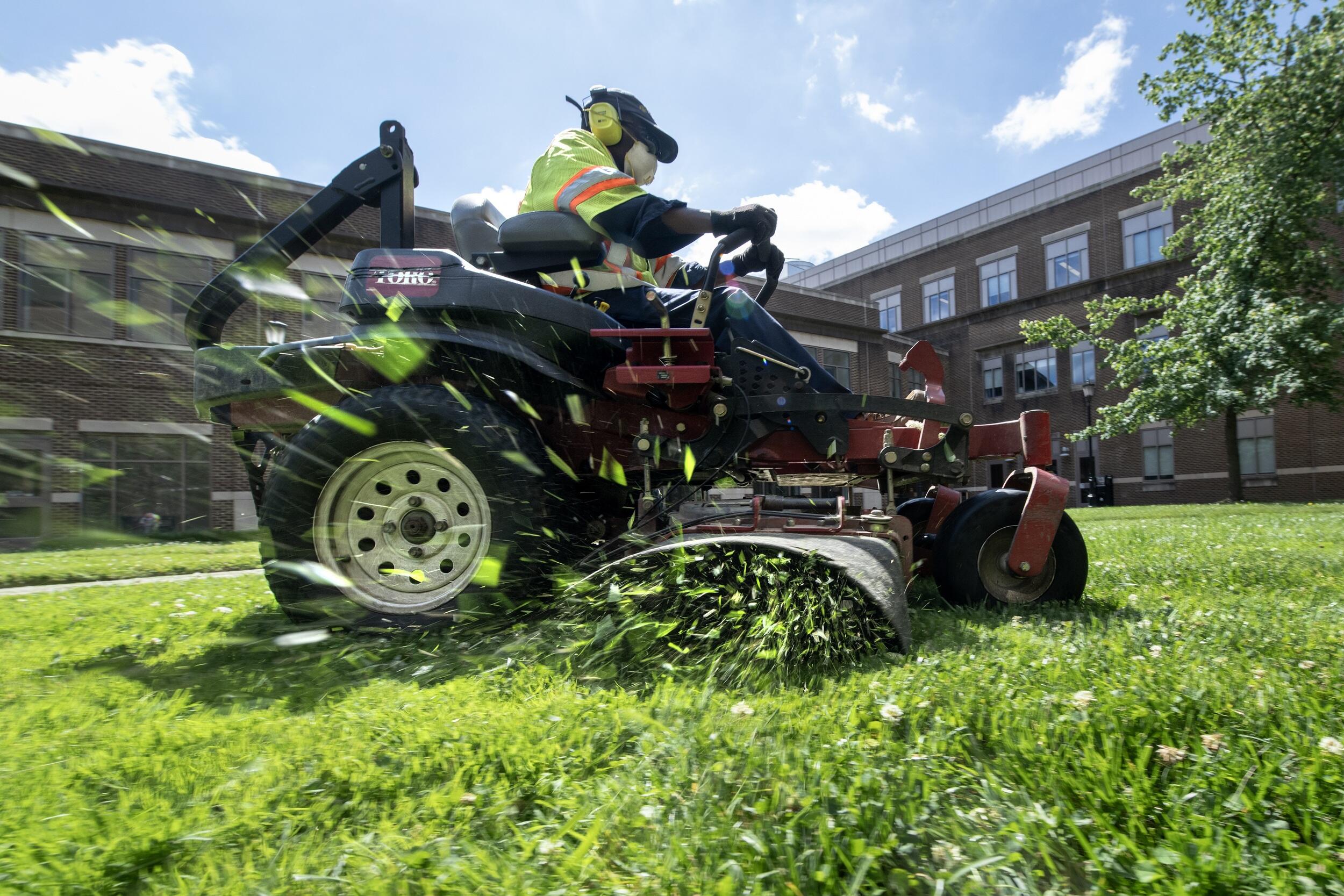A photo of a man cutting grass on a riding lawnmower. 