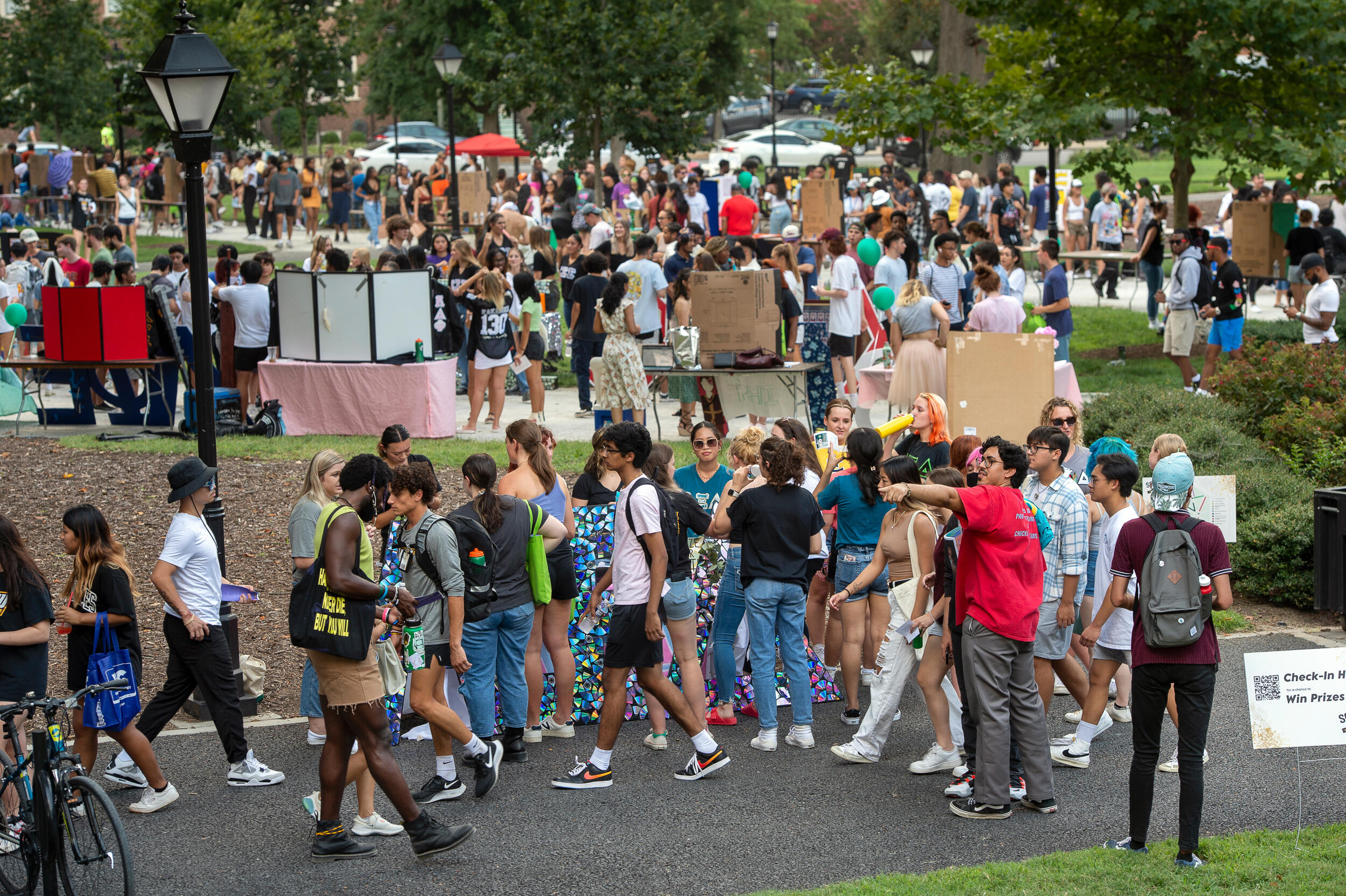 Hundreds of students walk around the sidewalks next to a tree-lined green space in Monroe Park.