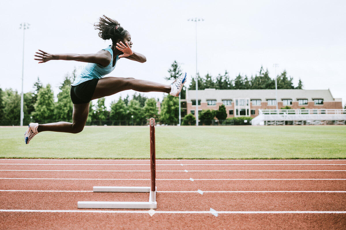 A woman jumping over a hurdle on a track field 