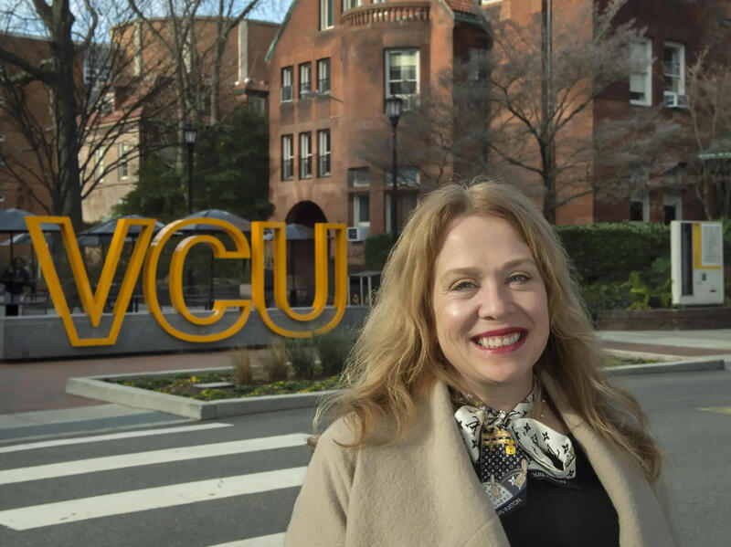 A woman smiles in front of a street and a yellow VCU sign.
