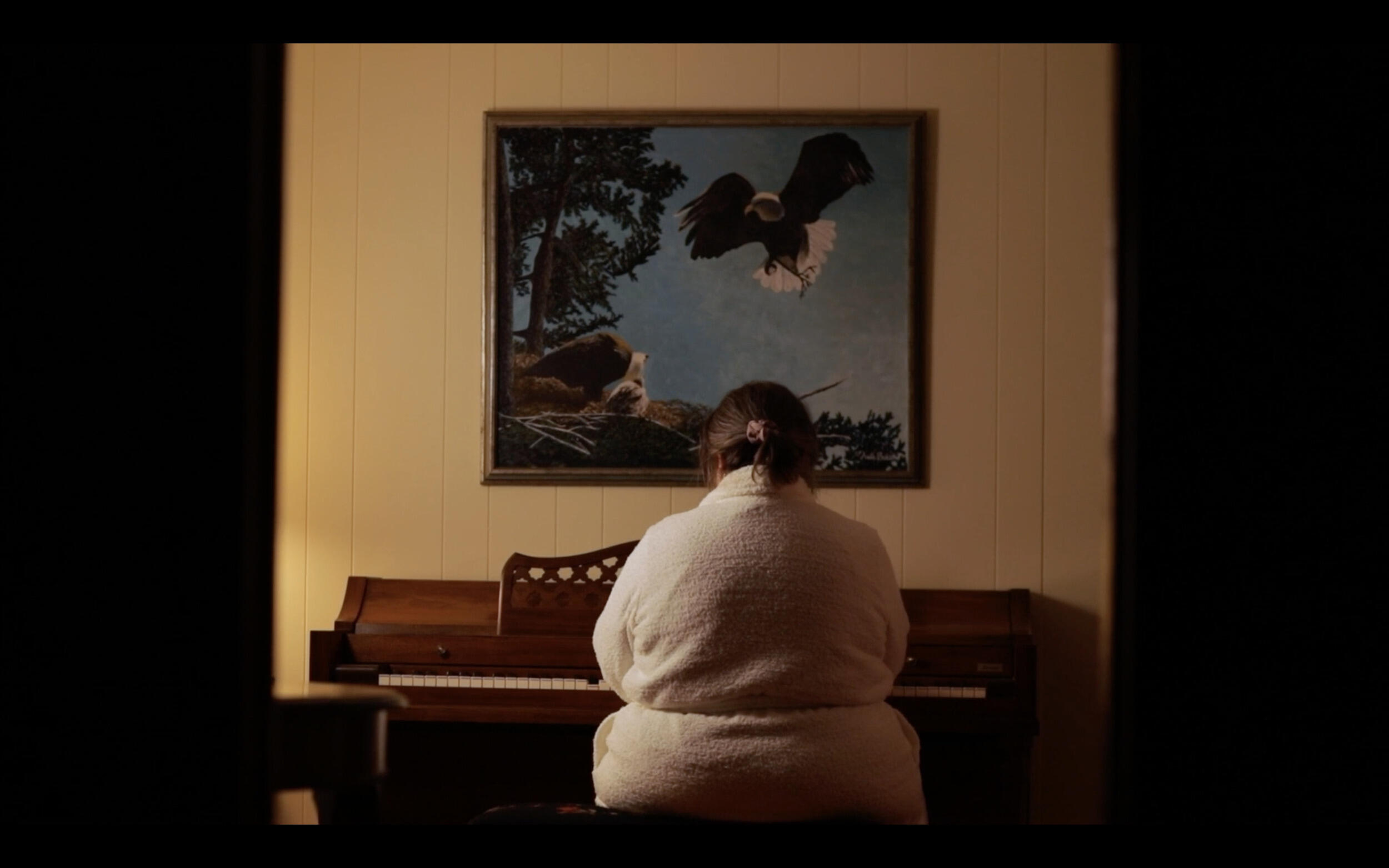A woman sitting at a piano. IN front of her is a painting of and eagle flying next to a cliff. 
