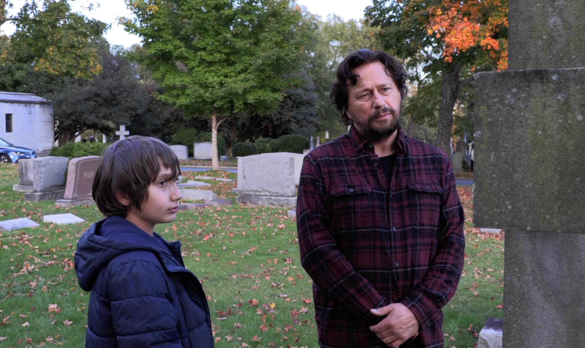 A man and a young boy standing in a cemetery 