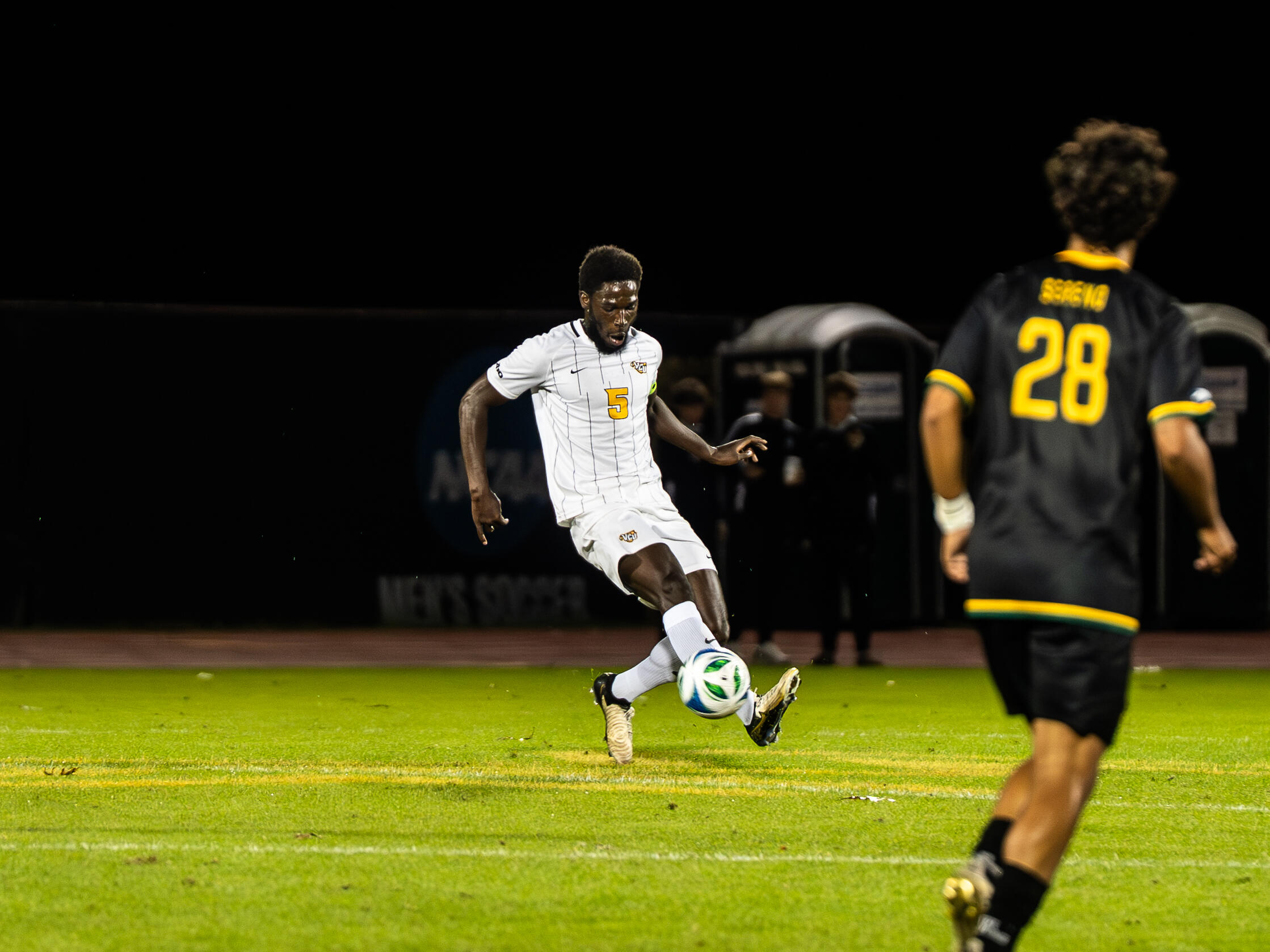 A man in a white uniform controls a soccer ball during a night game.