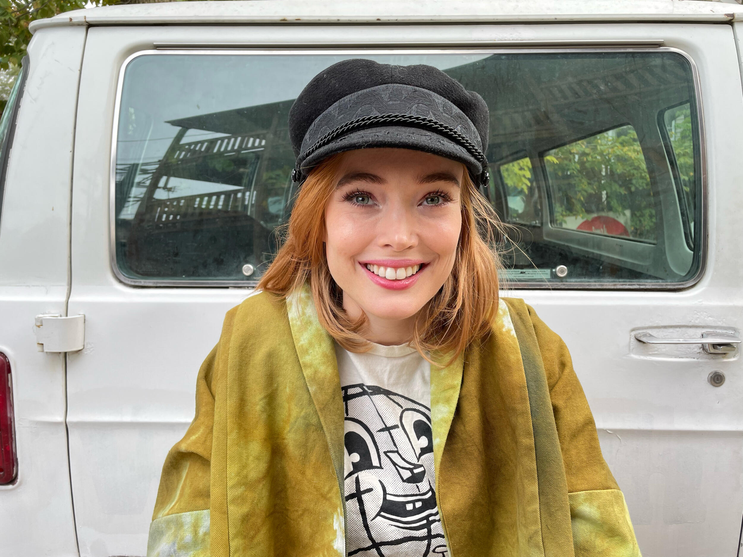 A woman wearing a paper boy hat and yellow jacket smiling 