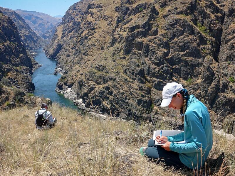 Two students seated on a bluff overlooking a river valley.