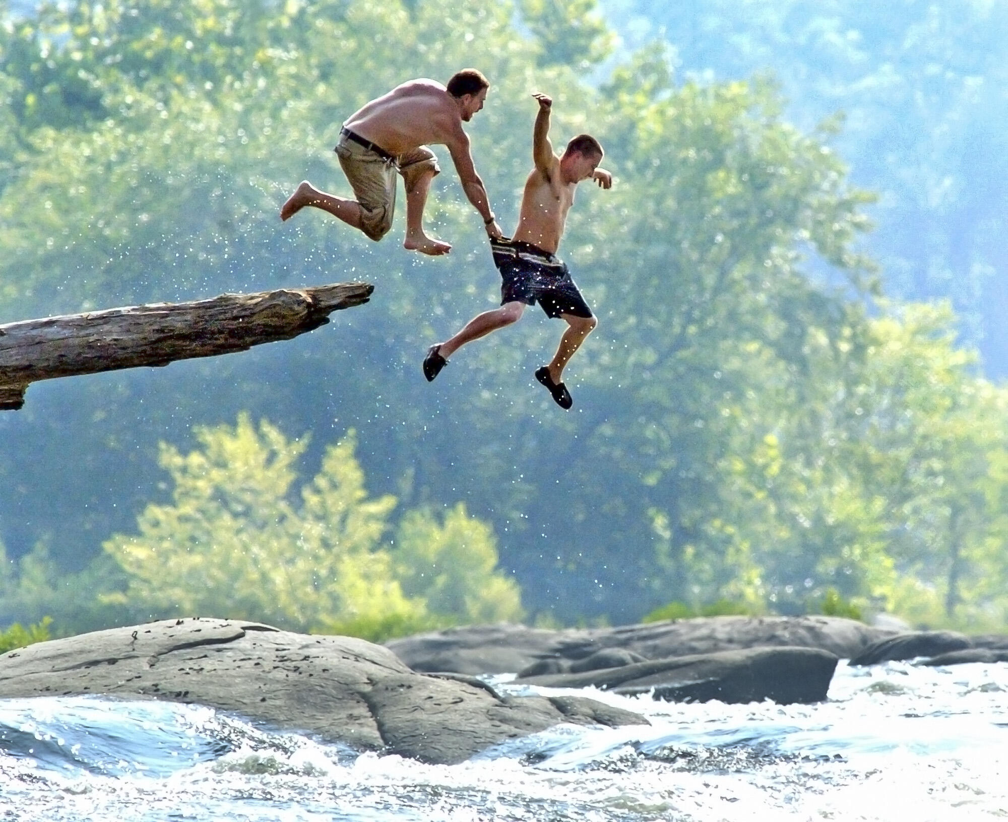 A photo of two men jumping off a rock into a river