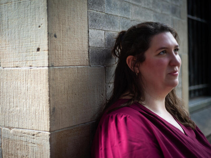A photo of a woman standing against a wall from the shoulders up. 
