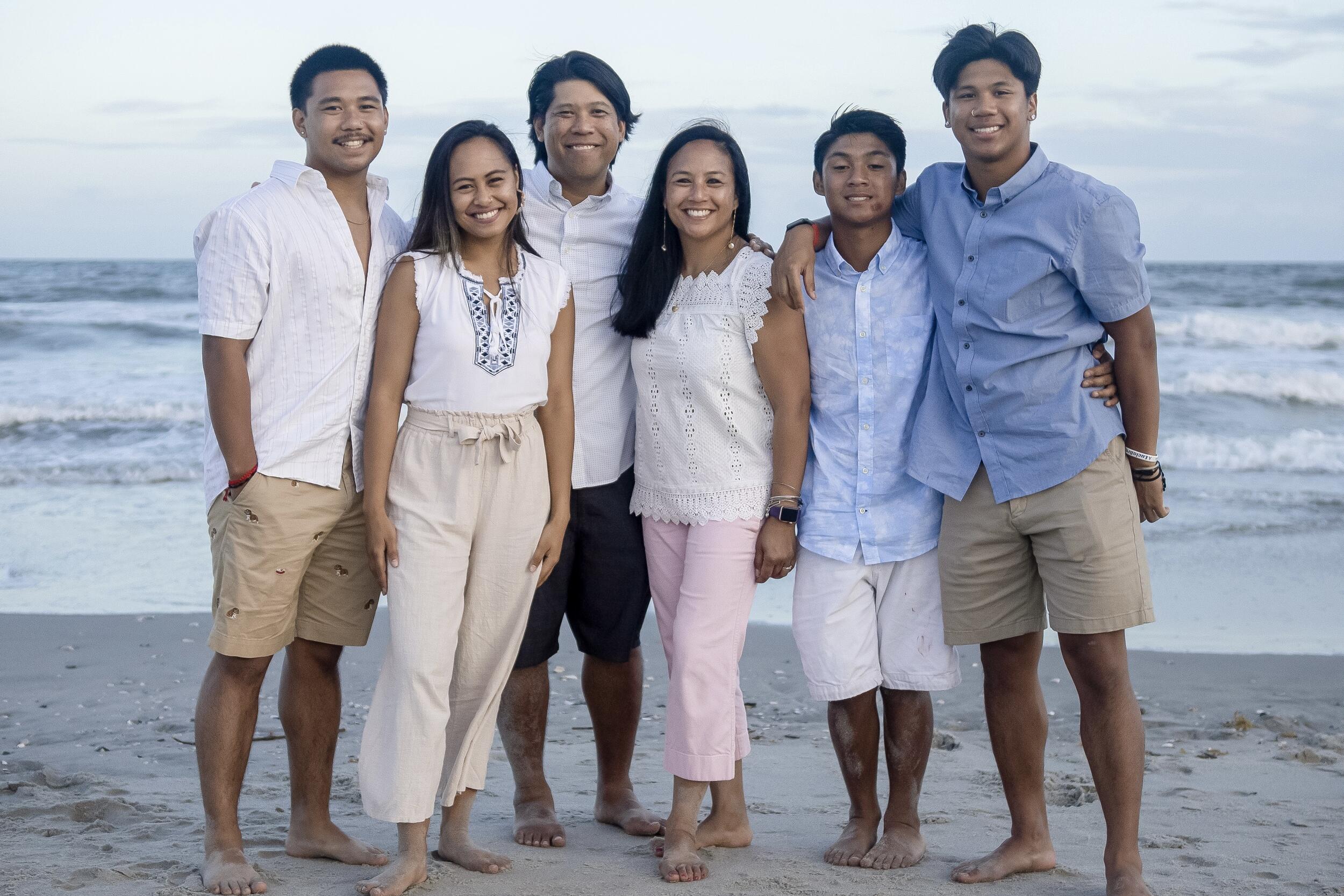 A group photo of six people standing on a beach. 