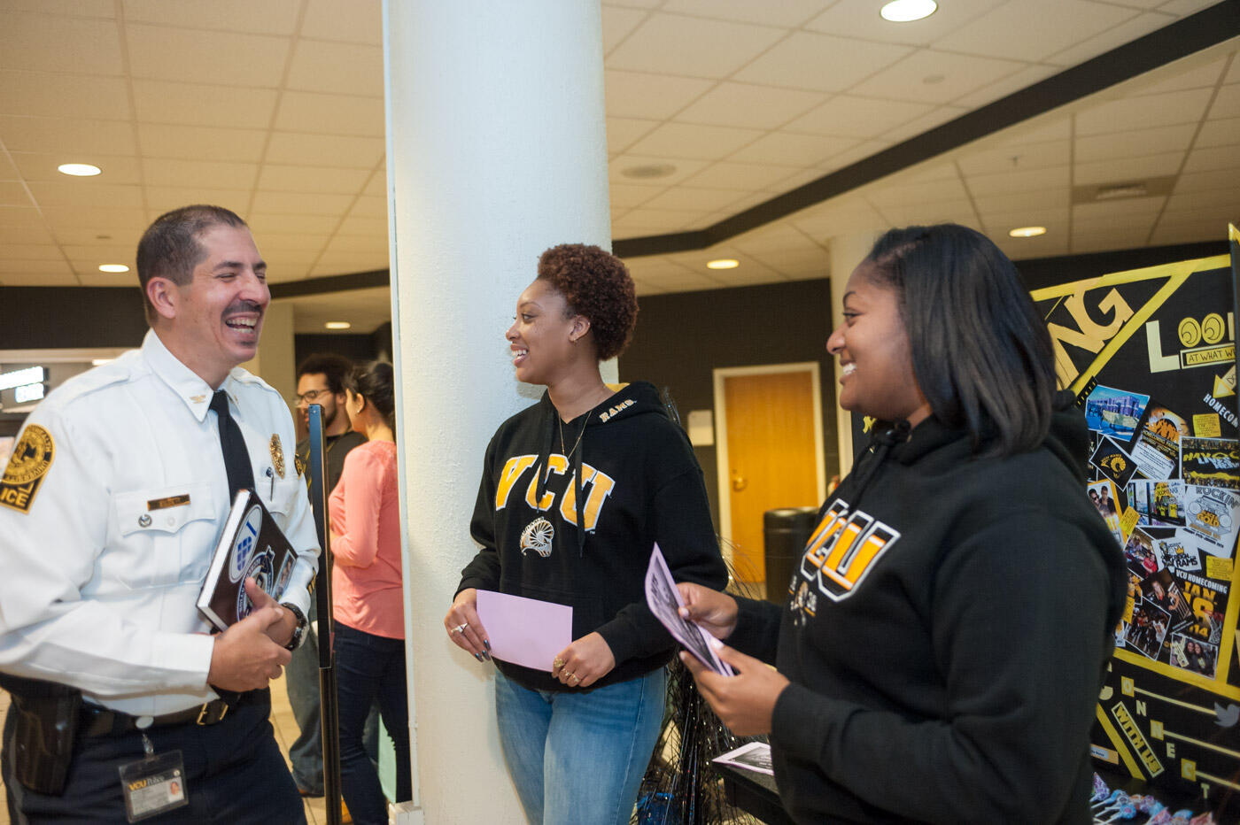 A photo of a man wearing a white police uniform shirt and black pants laughing with two women to his right. 