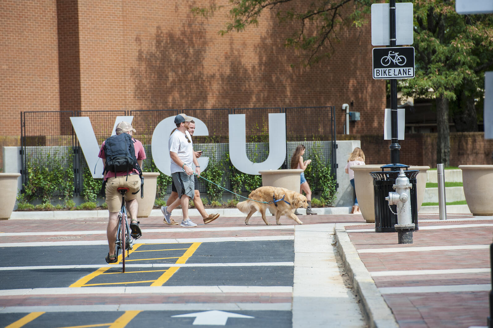 A bicyclist and pedestrians traversing the Monroe Park Campus at the corner of Linden and Grove streets.