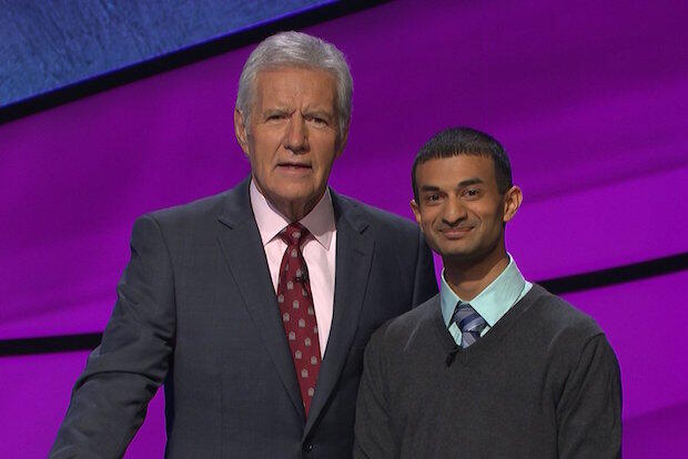 Two men stand in front of a purple background.
