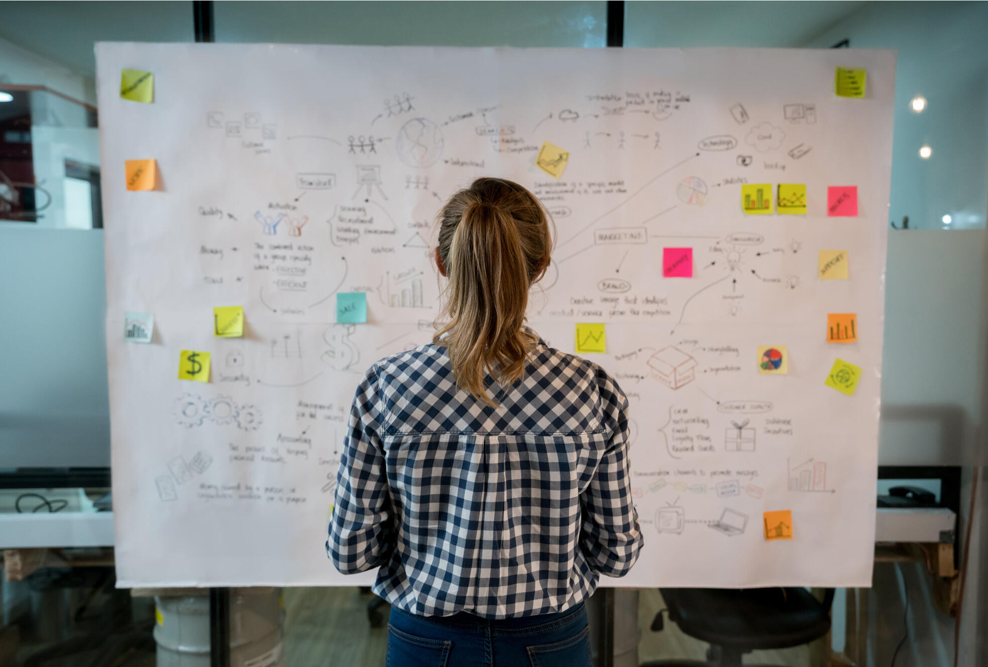 A photo of a woman looking at a board with words written on it and arrows. 